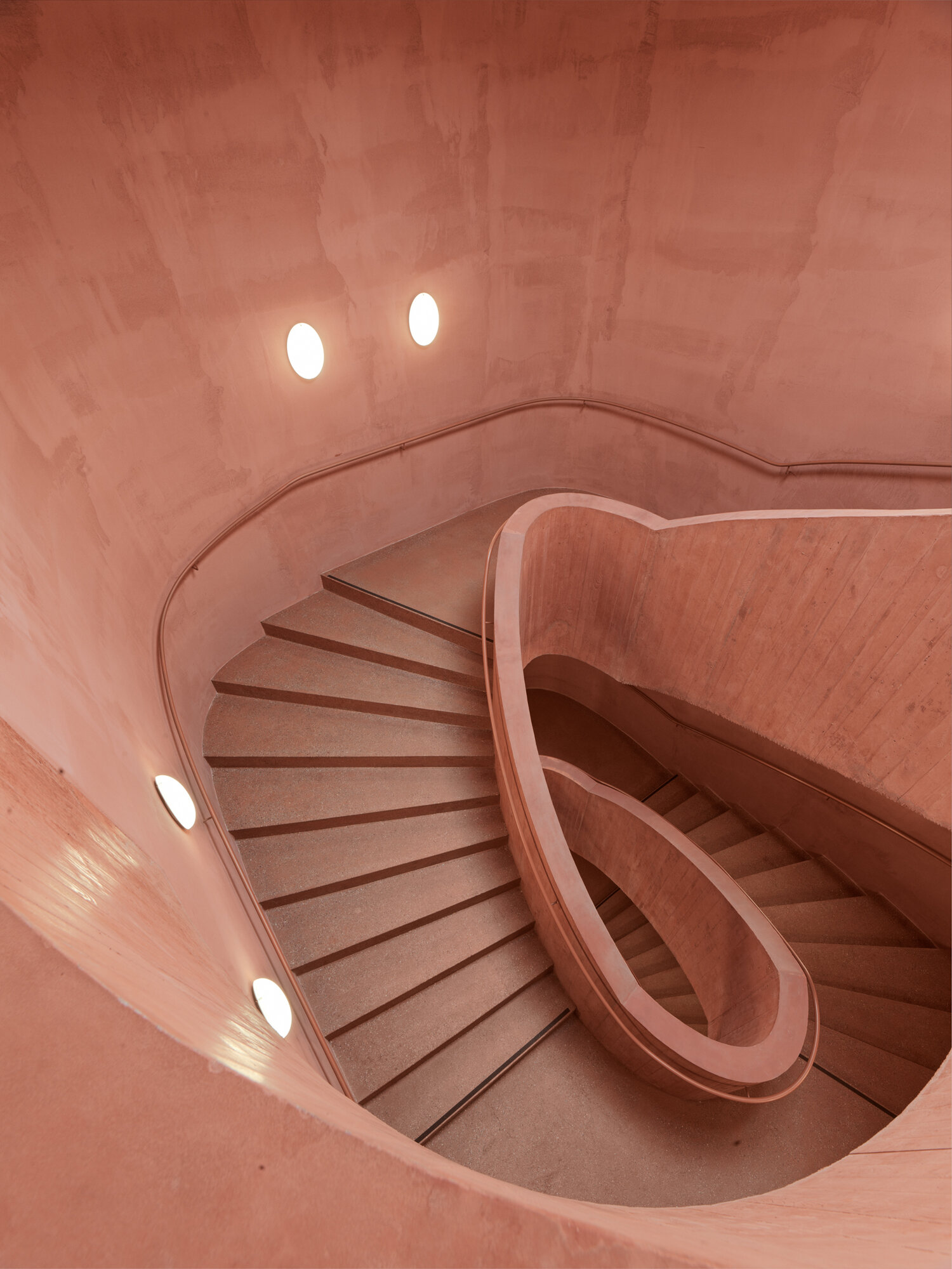 Das Treppenhaus beeindruckt mit seinem einzigartigen Design, das durch den Einsatz von rot eingef&auml;rbtem Beton gepr&auml;gt ist.