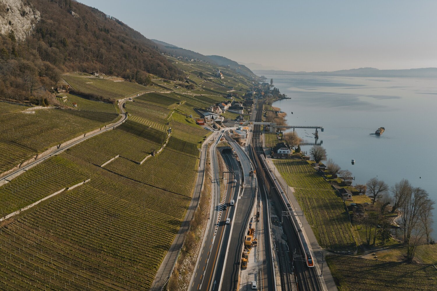 Die Luftaufnahme zeigt die Baustelle des Doppelspurausbaus zwischen Neuch&acirc;tel und Biel. Die Arbeiten erfolgen direkt neben der bestehenden Bahnlinie, auf der t&auml;glich rund 180 Z&uuml;ge verkehren. Der Bau verlangt eine pr&auml;zise Abstimmung zwischen Bahnbetrieb, Bauarbeiten und Sicherheitsanforderungen. Gleichzeitig sch&uuml;tzen umfangreiche Massnahmen die angrenzenden Natur- und Uferbereiche entlang des Bielersees. Die Aufnahme macht sichtbar, wie eng Infrastruktur, Landschaft und Siedlungsraum an diesem Standort miteinander verflochten sind. &copy; SBB CFF FFS, Stand 03.2026.